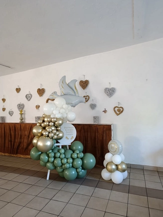 Ścianka do zdjęć na komunię z gołębiem, elegancka dekoracja sali na sztaludze, balony białe i złote z zielenią.